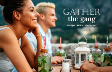 Guests enjoy drinks with mountain views on a terrace, surrounded by greenery and outdoor lanterns at a picturesque hotel.
