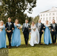 Wedding party on lush hotel lawn with elegant manor backdrop, featuring bridesmaids in blue dresses and groomsmen in suits.
